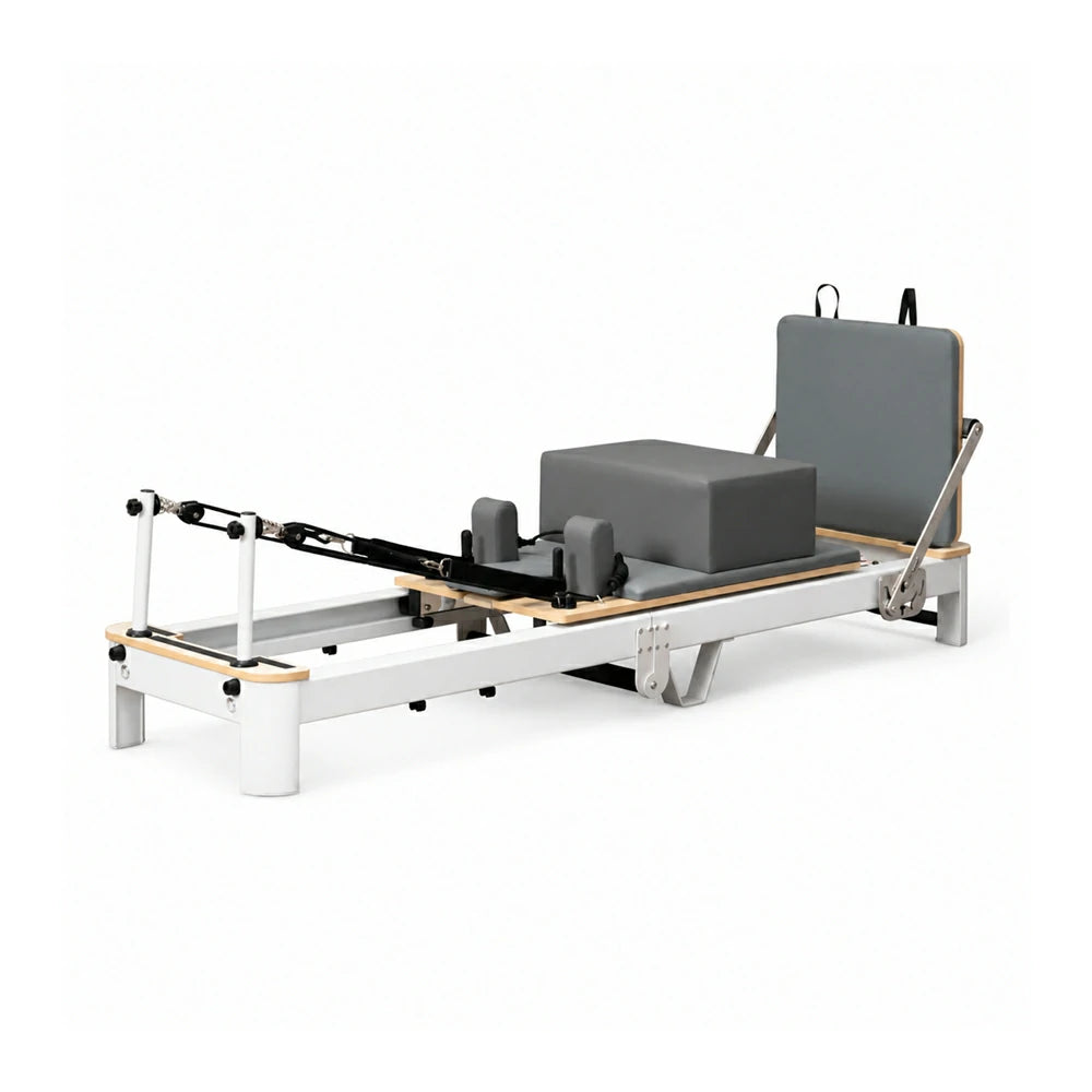 Pilates reformer machine with a white metal frame, natural wood accents, gray padded foam block, and gray backrest, shown on a clean white background.
